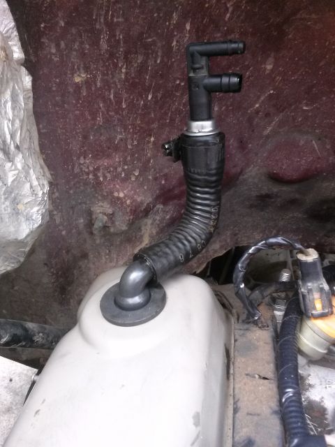 1996 Ford Bronco - A close-up view of a black plastic vacuum hose assembly connected to a light-colored plastic tank in what appears to be an engine bay. The…