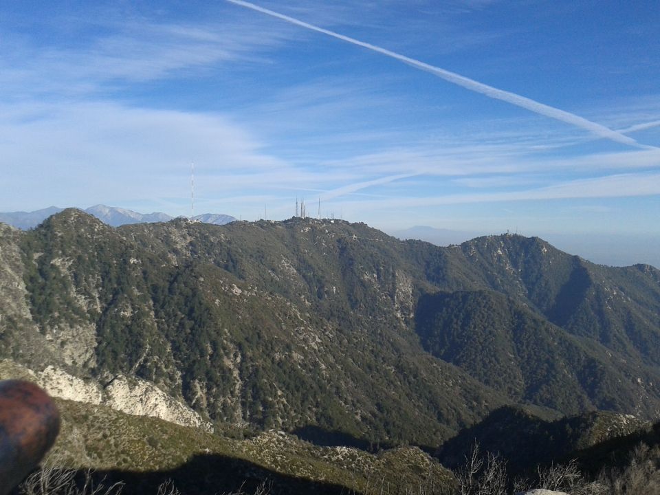 Mountain range with communication towers under a blue sky with contrails.