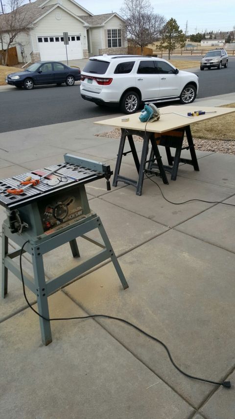 1996 Ford Bronco - A table saw and a workbench with tools are set up on a concrete driveway in front of a house. Two cars are parked on the street, and a whit…