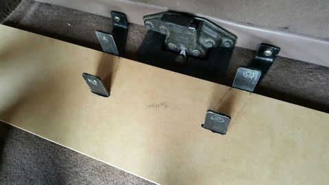 1996 Ford Bronco - A piece of particle board is placed over a vehicle's carpeted floor, with metal brackets attached to the vehicle's frame protruding through…