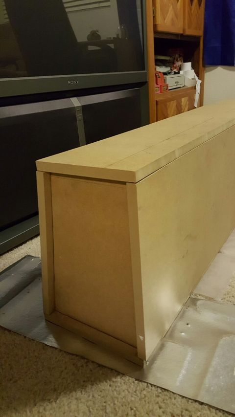 1996 Ford Bronco - A long, light brown wooden cabinet or shelf unit is positioned on a carpeted floor, partially obscuring a large black television screen wit…