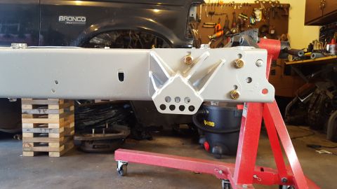 1994 Ford Bronco - A silver-painted custom bracket is bolted to the frame of a dark-colored Ford Bronco. The vehicle is supported by wooden pallets and a red…