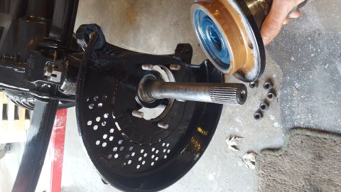 1994 Ford Bronco - A close-up of a vehicle's front wheel hub assembly, with the brake rotor and spindle visible. A greased bearing assembly is being held abov…