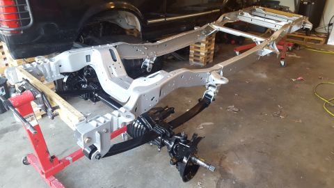 1994 Ford Bronco - A vehicle frame, likely from a 1994 Ford Bronco, is shown in a garage setting. The frame has been painted silver and features a black suspe…