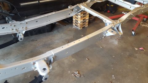 1994 Ford Bronco - A silver painted vehicle frame is shown in a garage setting. The frame is supported by wooden blocks and red jack stands.