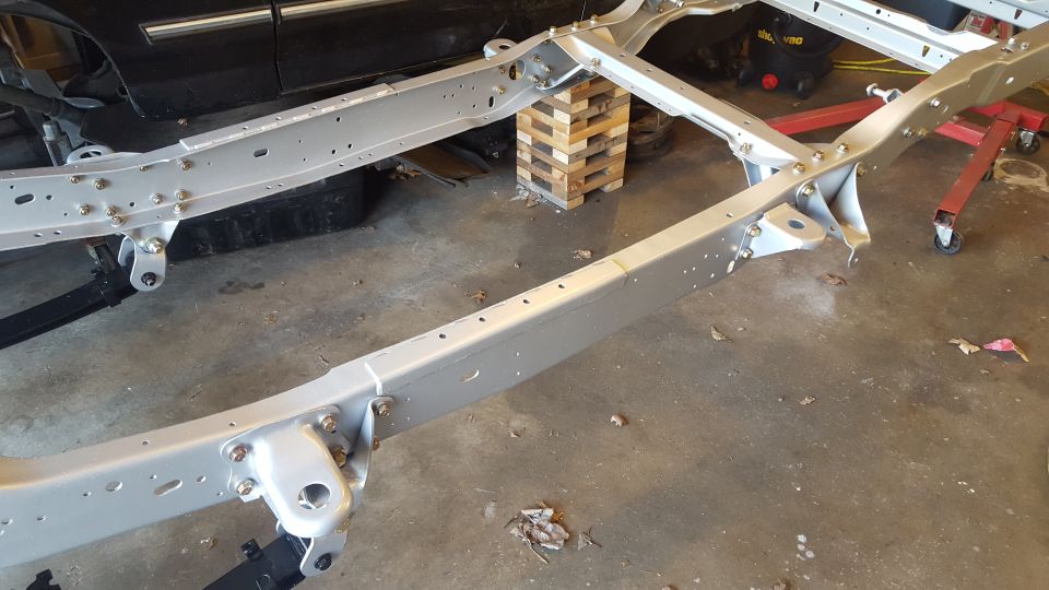 Silver painted vehicle frame supported by blocks and jack stands in a garage.