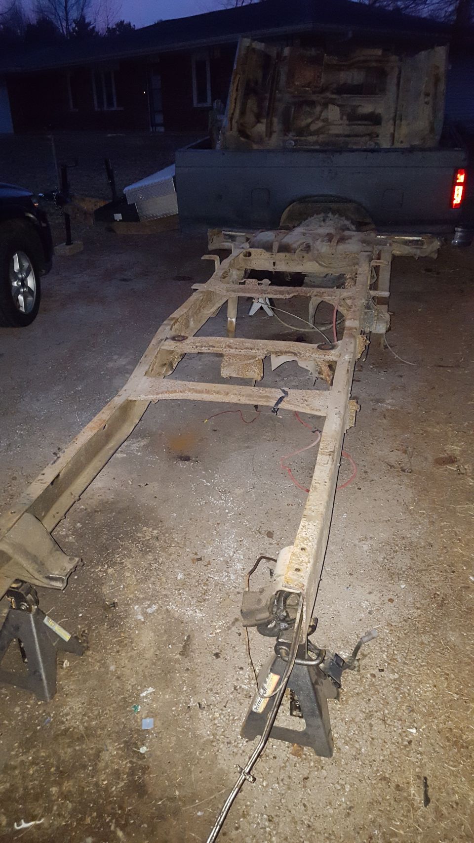 Rusted truck frame on jack stands, pickup truck bed in background