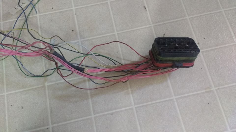 Wiring harness with black connector and colorful wires on a tiled floor.