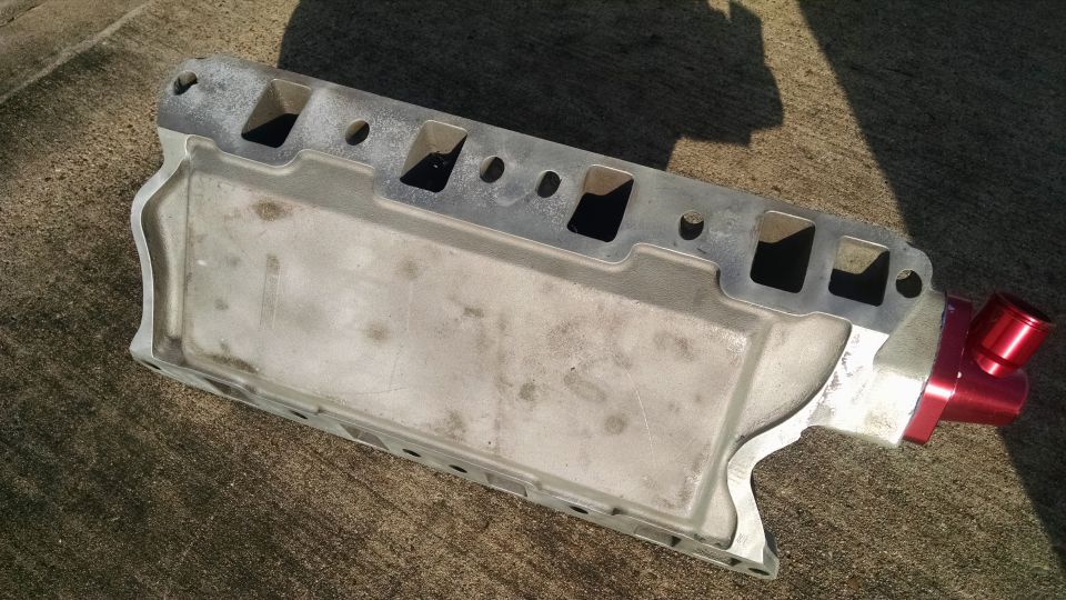 Silver aluminum intake manifold with red fitting on concrete