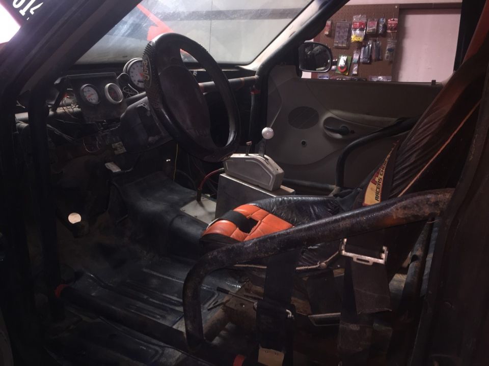 Interior of a modified vehicle with roll cage, racing seat, shifter, and gauges.