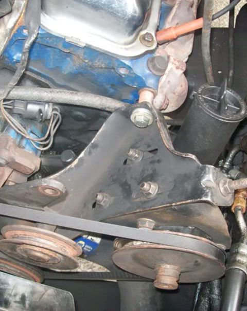 1978 Ford Bronco - A close-up view of a V-belt system and mounting bracket on a vehicle's engine. The bracket is black metal and attaches to a blue-painted en…