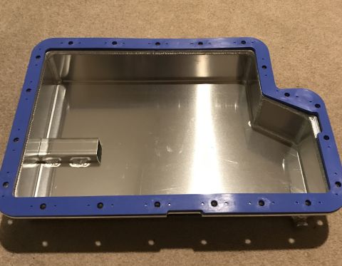 1995 Ford Bronco - A shiny metal oil pan with a blue gasket is shown on a carpeted surface. The oil pan has a rectangular tube welded inside and numerous bolt…