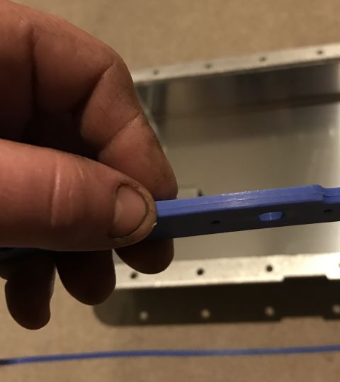1995 Ford Bronco - A person's hand is holding a blue plastic part with holes in it over a metal enclosure with many small holes. The enclosure appears to be a…