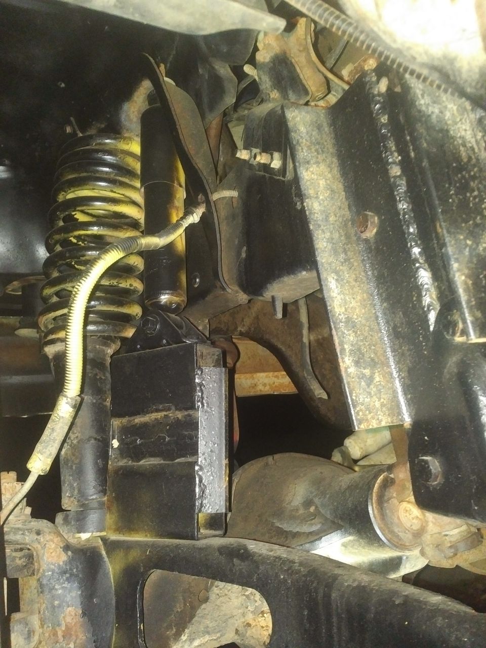 1980 Ford Bronco suspension with yellow coil spring shock absorber and black metal parts.