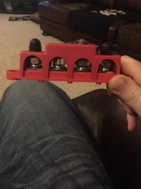 1982 Ford Bronco - A person is holding a red automotive power distribution block with four silver terminals and black protective caps. The block is mounted on…