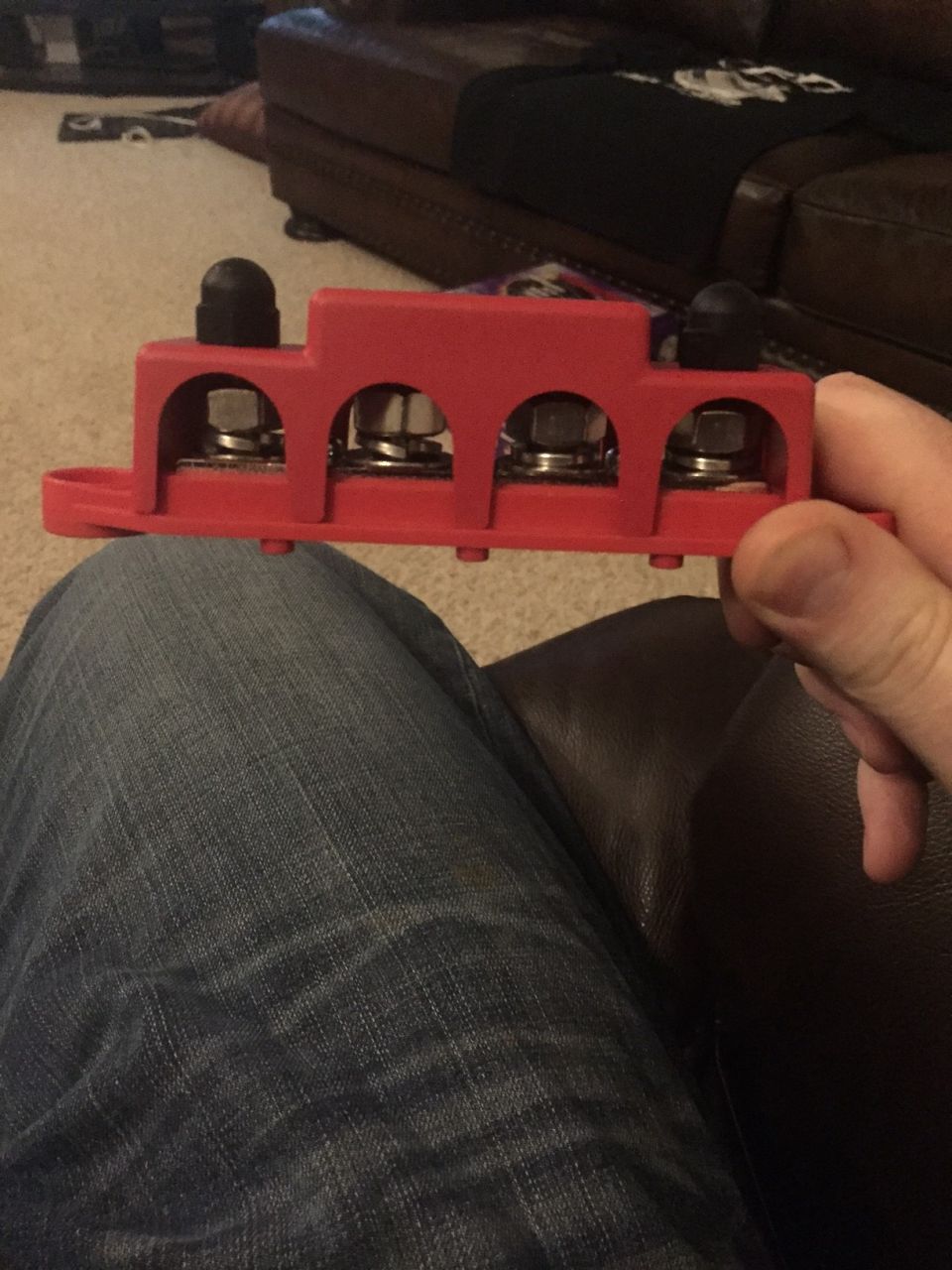 Red automotive power distribution block with four terminals and black caps.