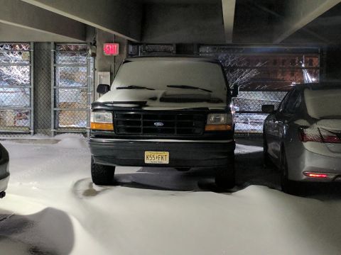 1995 Ford Bronco - A black Ford Bronco covered in snow is parked in a dimly lit garage with snowdrifts on the ground. The vehicle's license plate reads "K55 F…