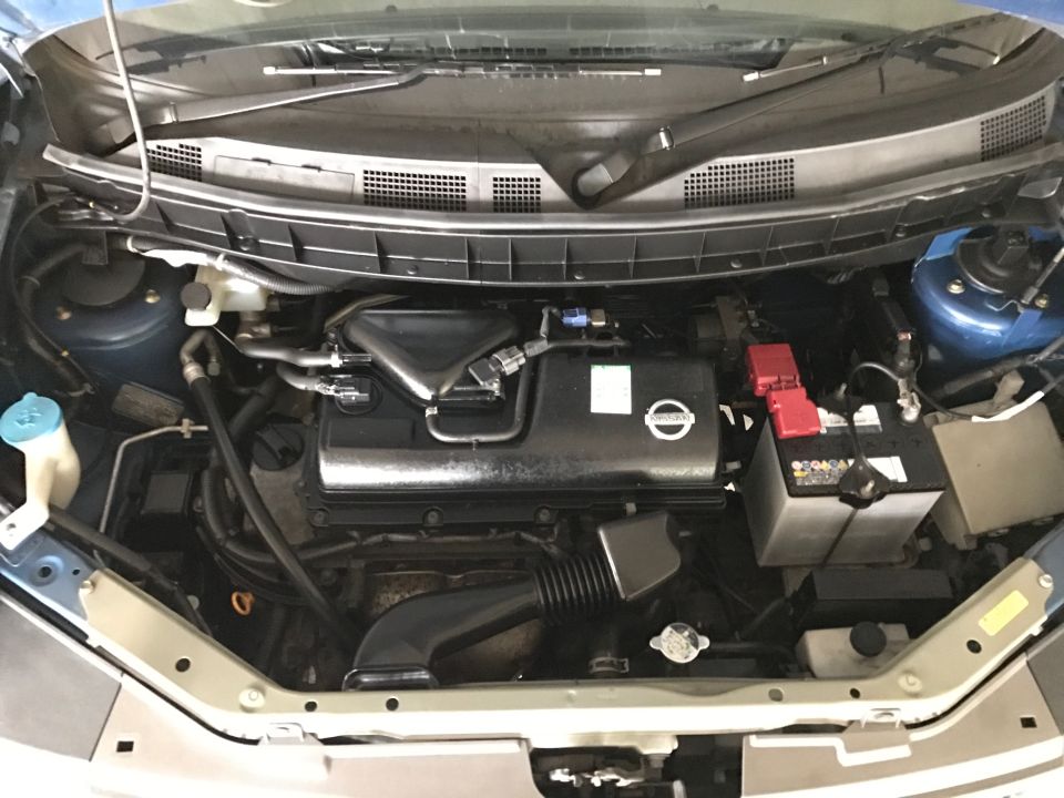 Engine bay of a Nissan Cube with engine, battery, and reservoirs visible.