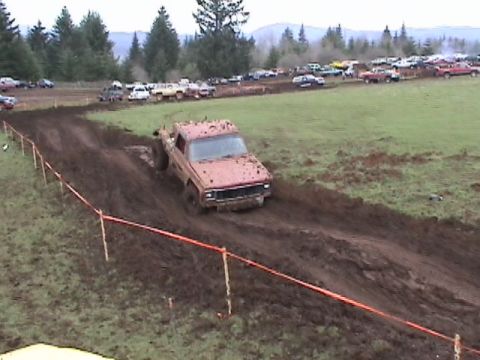 1994 Ford Explorer - Pickup truck navigates a muddy course during an event with spectators and other vehicles present.