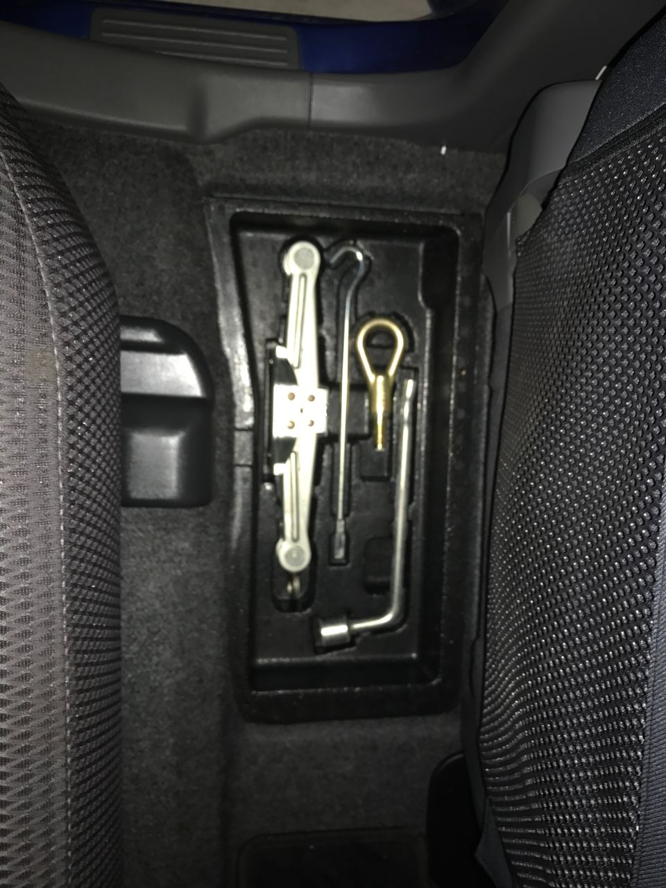 Car jack and lug wrench in a vehicle's storage compartment.