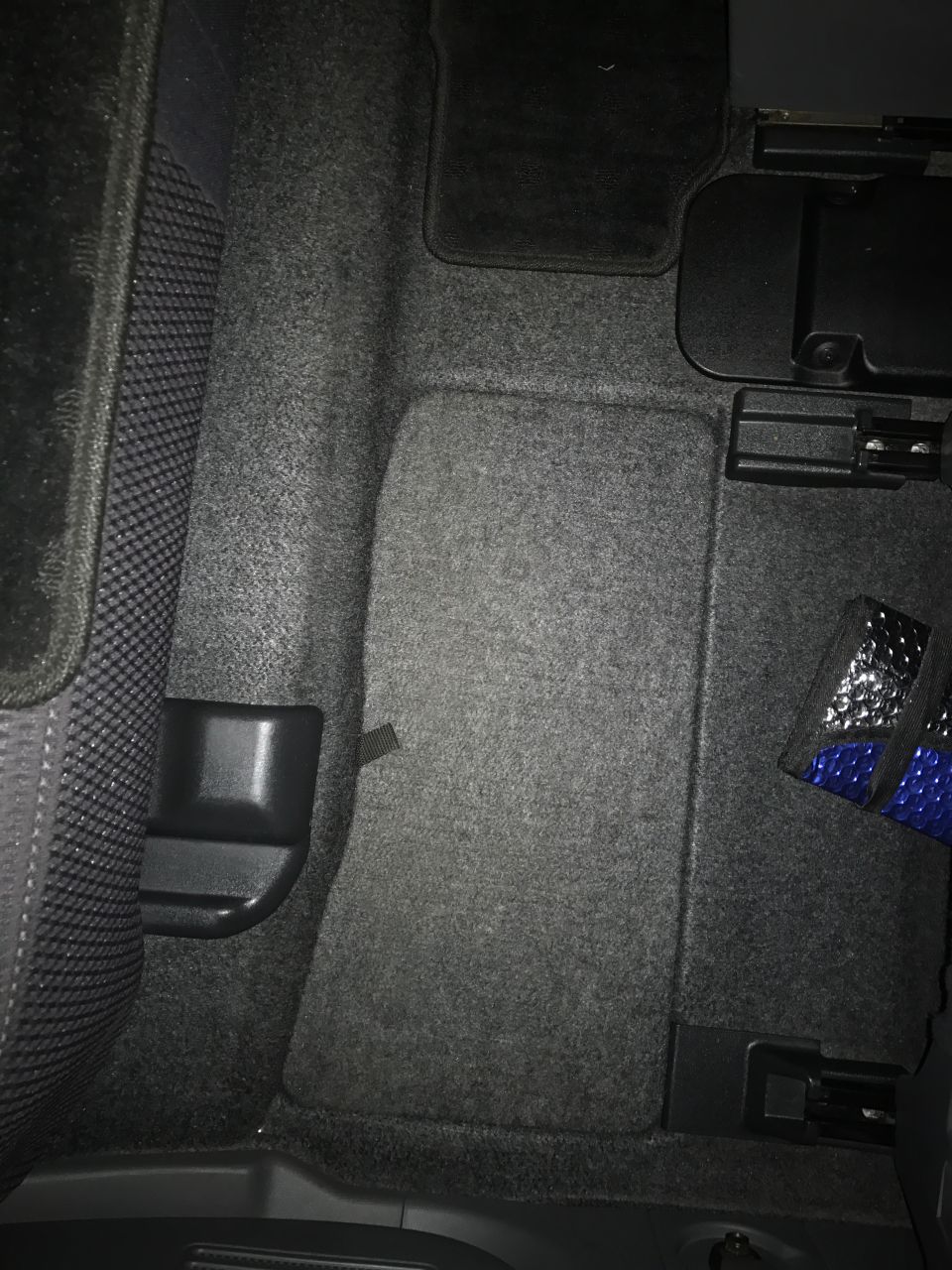 Car interior showing carpeted floor and rear seat area with black seatbelt anchor.