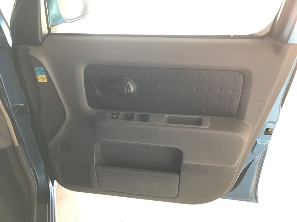 Interior door panel of a blue car, showing door handle, window controls, and storage.