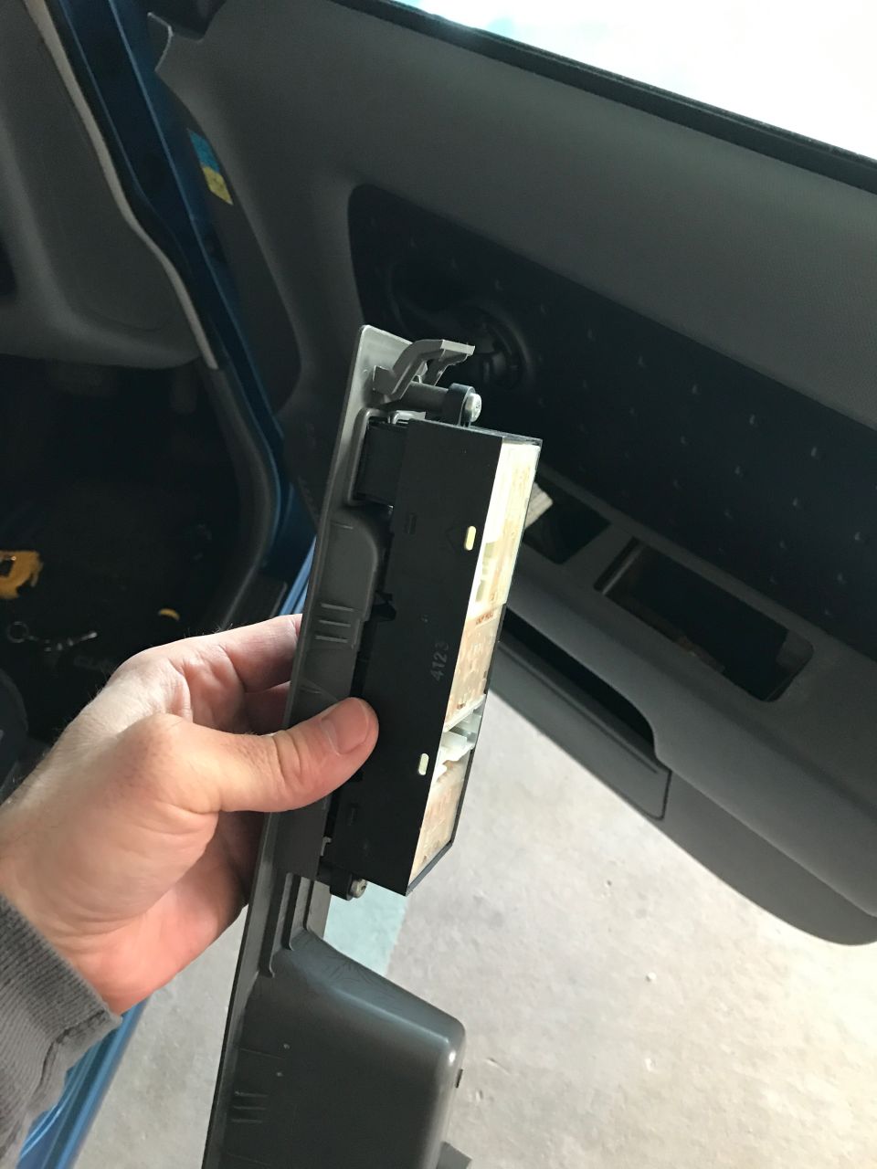 Hand holding a car window switch assembly, showing electrical components.