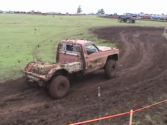 Mud-covered stripped square-body pickup racing a rutted mud bog course
