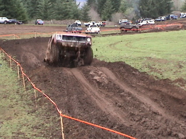 Mud-covered red SUV climbing out of a mud pit, front wheels lifting, bog course