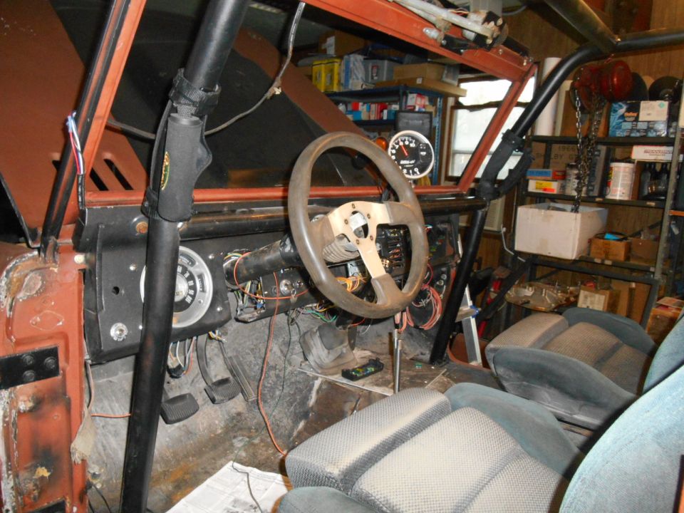 Interior of a modified Ford Bronco with roll cage, racing wheel, and seats.