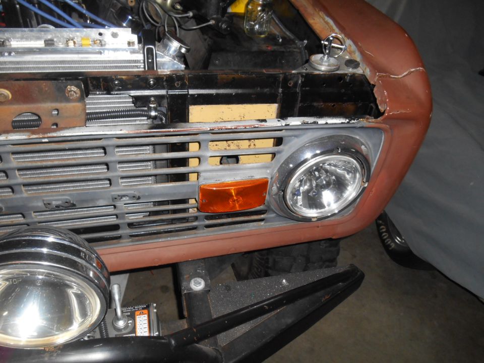 Front view of a vintage Ford Bronco grille, headlight, and fender with visible rust and modifications.