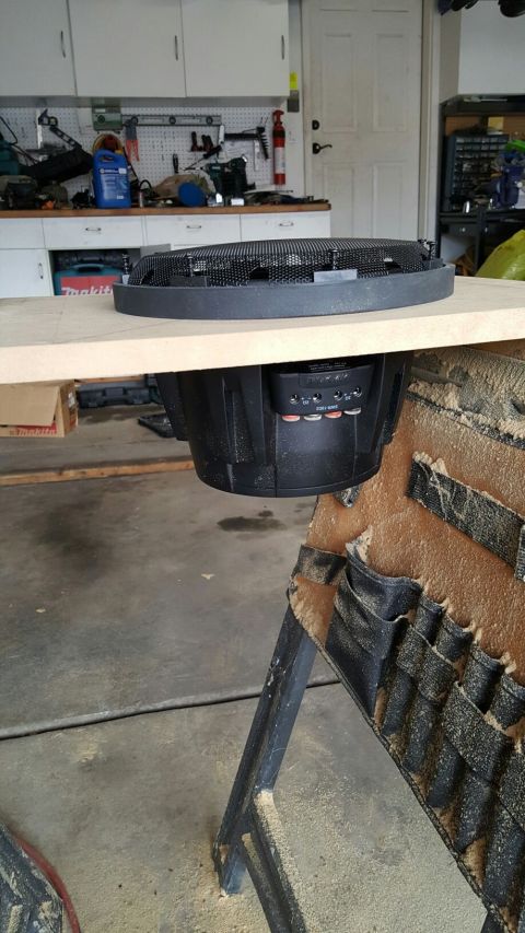 1996 Ford Bronco - A car subwoofer is mounted to a piece of wood, likely for installation in a vehicle. The subwoofer is black with a mesh grill on top and ap…