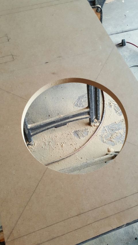 1996 Ford Bronco - A circular cutout is made in a piece of particle board, revealing a black metal structure and a pile of sawdust underneath. The board has s…