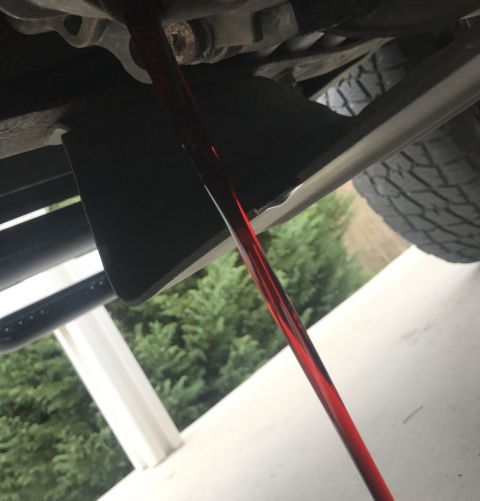 1995 Ford Bronco - Red fluid is draining from the underside of a vehicle, likely transmission fluid during a fluid change. The vehicle appears to be an SUV or…