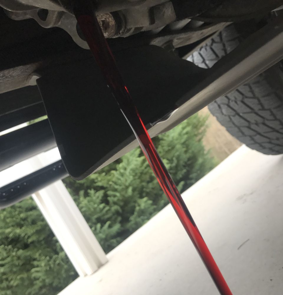 Red fluid draining from underside of a vehicle, likely during a fluid change.