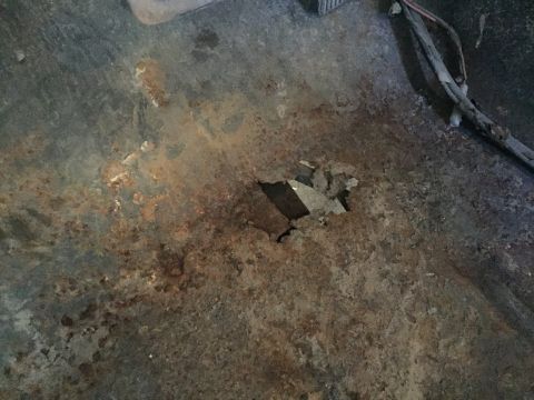 1979 Ford Bronco - A close-up view of heavily rusted metal, likely the floor pan of a vehicle, with a hole rusted through it. Wires are visible in the upper r…