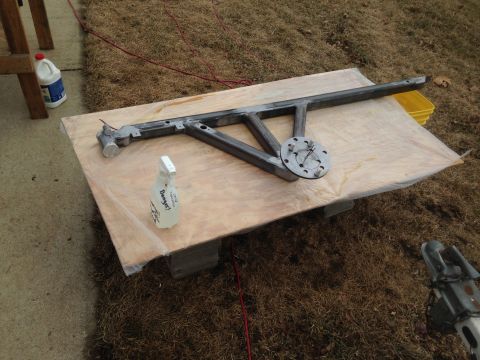 1979 Ford Bronco - A metal frame assembly is laid out on a plywood sheet placed on top of concrete blocks. A bottle of cleaner and a red cord are visible near…