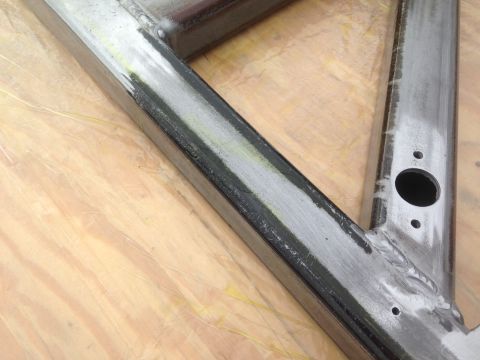 1979 Ford Bronco - A close-up view of a metal frame, likely part of a vehicle chassis, showing welded joints and a hole drilled through one of the tubes. The…