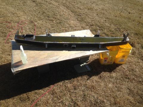 1979 Ford Bronco - A green metal bumper or frame part is laid out on a wooden surface outdoors, with two yellow buckets and a spray bottle nearby. A red cord…