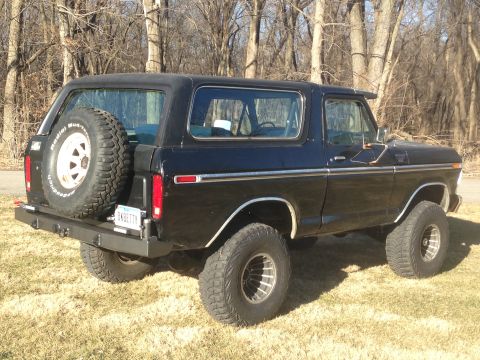 1979 Ford Bronco - The rear passenger side of a black 1970s Ford Bronco is shown parked on a grassy area with trees in the background. Visible modifications i…