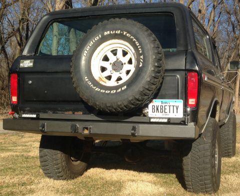 1979 Ford Bronco - The rear view of a black 1979 Ford Bronco with a spare tire mounted on the back. A custom bumper with trailer hitch receivers is installed,…