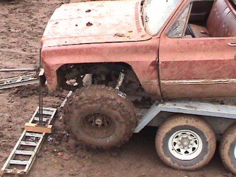 1994 Ford Explorer - A heavily modified and mud-caked red pickup truck is positioned on a trailer with large off-road tires.