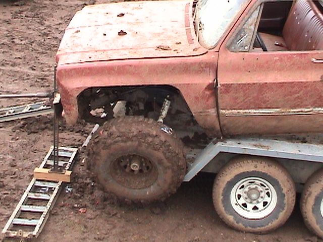 Muddy red 4x4 with fender removed loading onto a trailer at a mud event