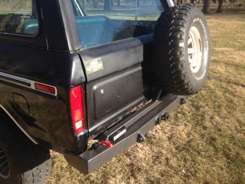 1979 Ford Bronco - The rear driver's side of a black 1979 Ford Bronco is shown, featuring a spare tire mounted on the back and a custom bumper with tow hitch…