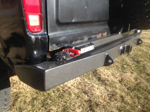 1979 Ford Bronco - A close-up rear view of a black pickup truck's aftermarket bumper with a trailer hitch receiver and tow hooks. A small LED light bar and a…