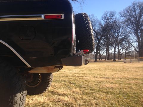 1979 Ford Bronco - A rear-side view of a black Ford Bronco shows its spare tire mounted on the back, along with a custom bumper and a red taillight. The vehic…