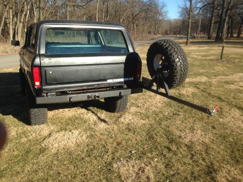 1979 Ford Bronco - The rear passenger side of a black 1979 Ford Bronco is shown parked on a grassy area with a spare tire mounted on a swing-away carrier exte…