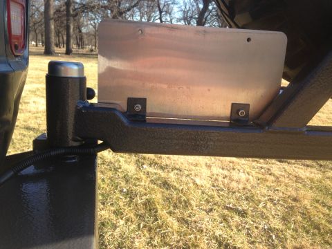 1979 Ford Bronco - A close-up view of a license plate bracket mounted to the rear of a vehicle, likely a trailer hitch assembly. The bracket is made of metal…