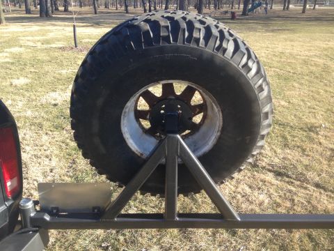 1979 Ford Bronco - A rear-mounted spare tire on a custom swing-away carrier is shown on the back of a vehicle. The tire is large and aggressive, with a rugged…