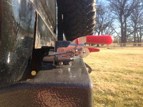 1979 Ford Bronco - A close-up view of a toggle clamp with red handles attached to the frame of a vehicle, possibly a Ford Bronco. The clamp is silver and red,…